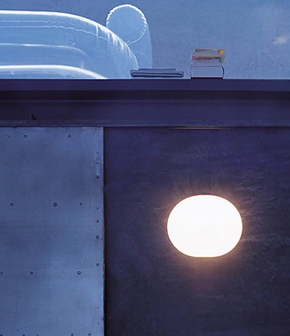 Flos Glo-Ball wall sconce illuminates a dark wall with books stacked on top.