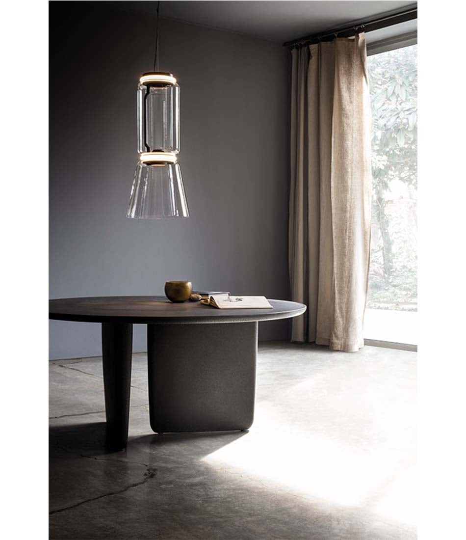 Flos Noctambule suspension lamp above a wooden table. Glass cone shade with glass cylinder body.