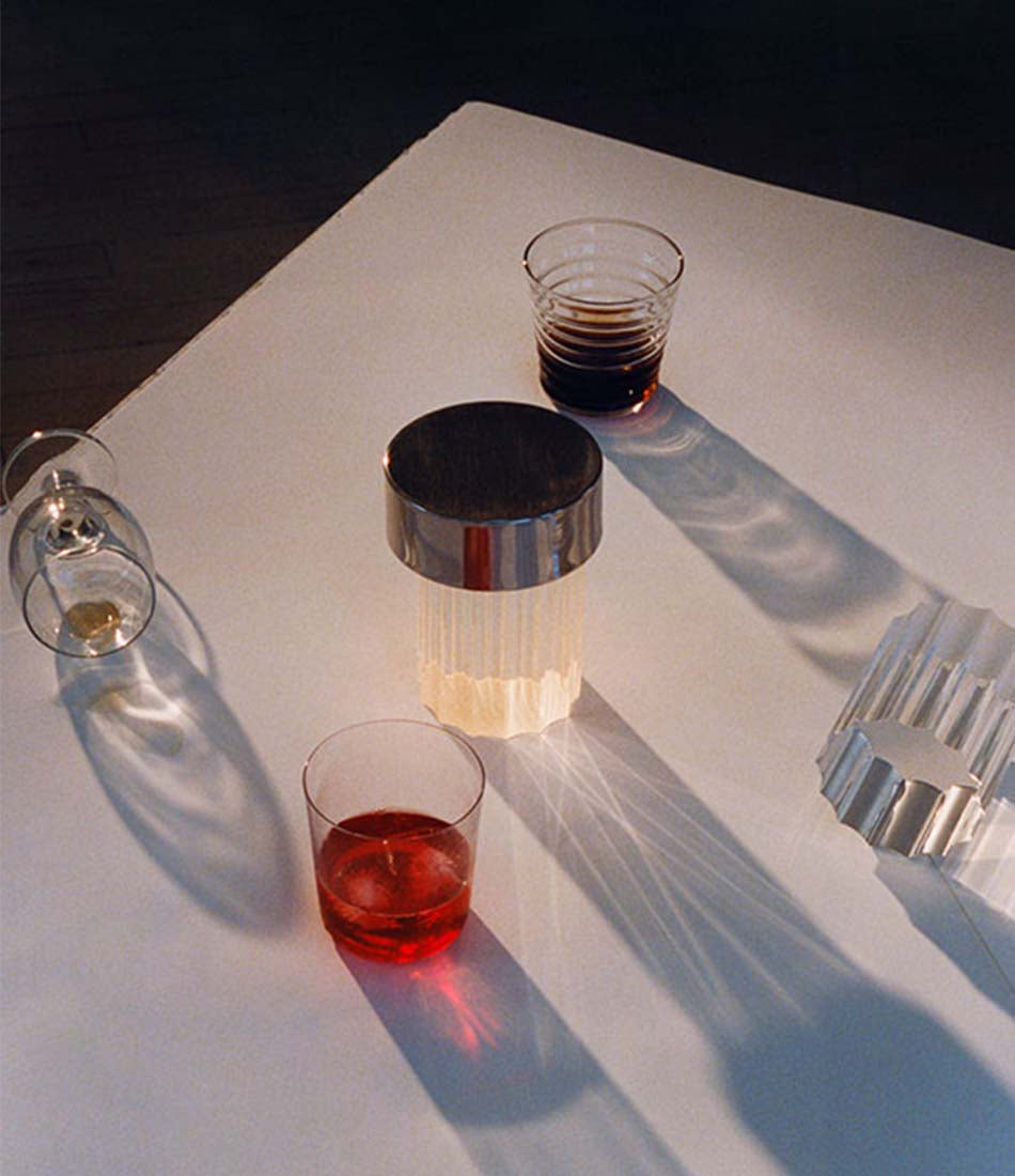 Flos Last Order table lamp next to two cocktail glasses and an overturned wine glass on a table.