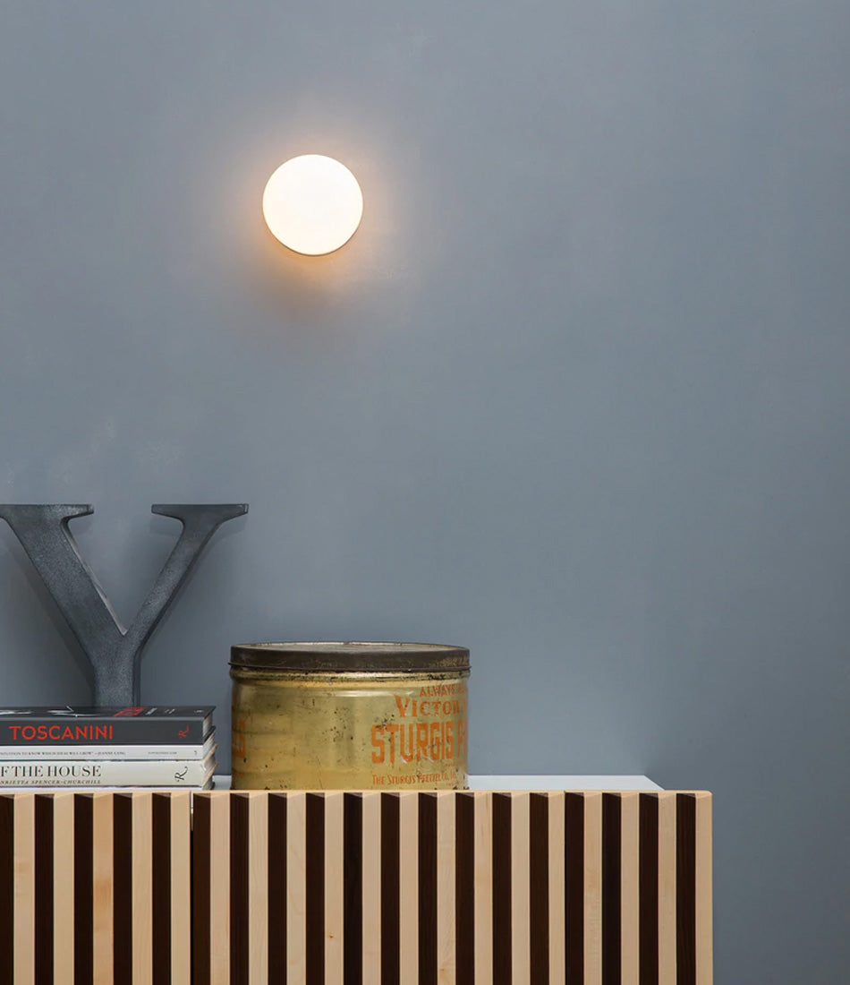 Flos Mini Glo-Ball wall lamp fixed to the wall above a sideboard containing books.