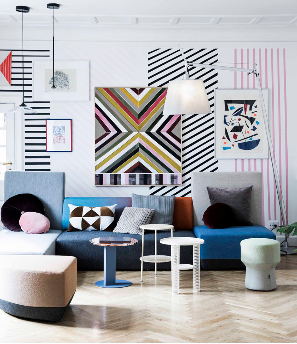 Artemide Tolomeo Maxi floor lamp next to a sectional in front of a patterned wall.