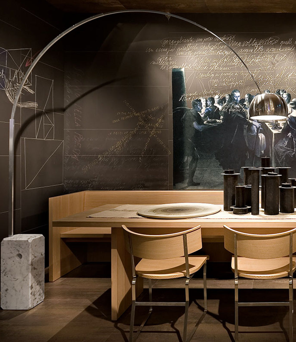 Flos Arco floor lamp positioned overtop a wooden dining table containing ornamental vases.