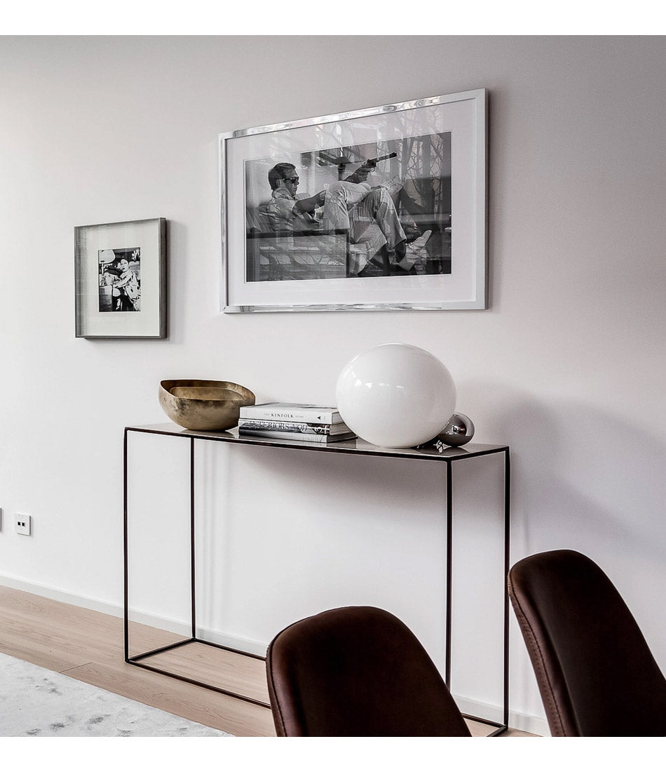 Flos Copycat table lamp on a console beneath a large portrait.