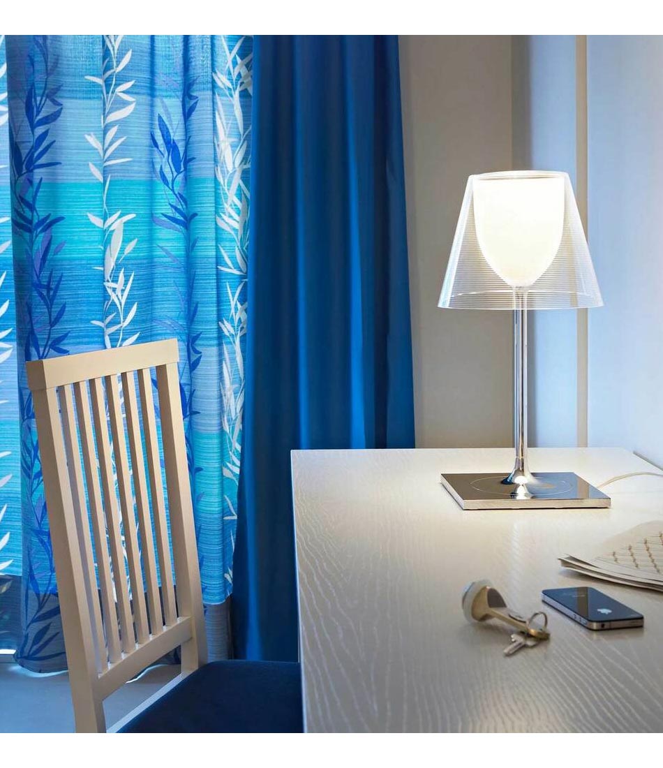 Flos KTribe table lamp with transparent lampshade on a white wooden desk.