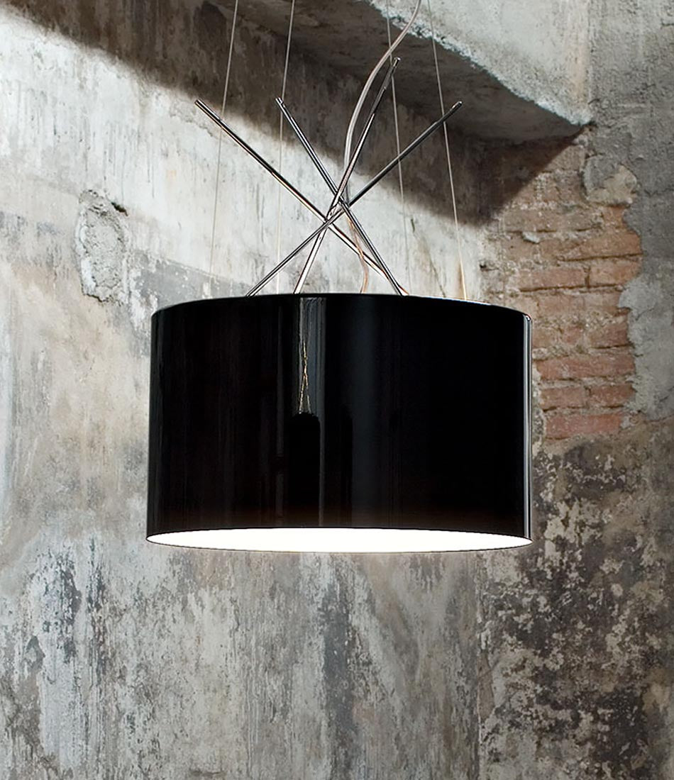 Glossy black Flos Ray suspension lamp hanging in front of worn concrete and brick wall.