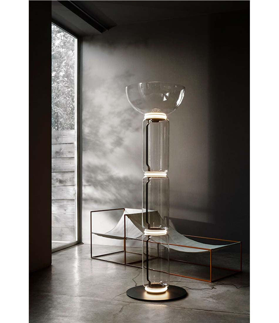 Flos Noctambule floor lamp. Glass bowl top with 3 glass cylinder body next to a sculpture.