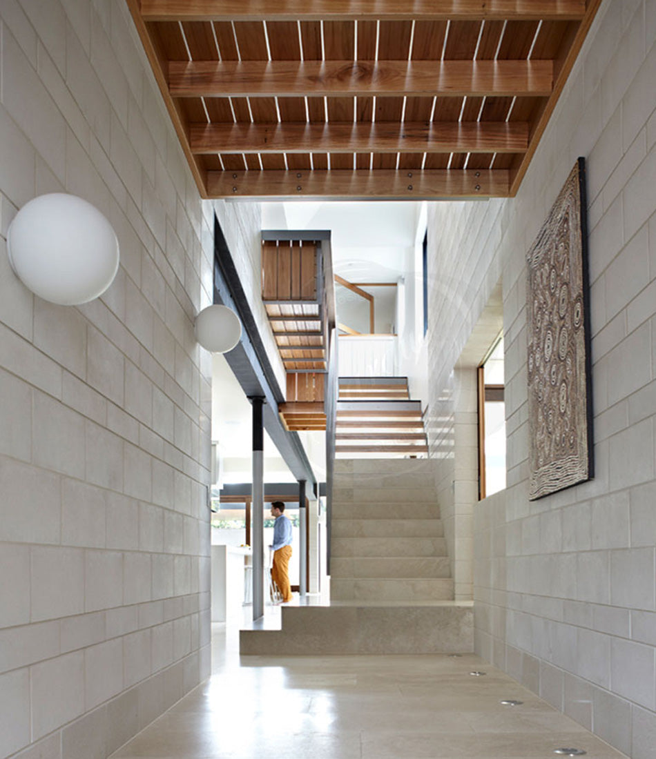 Two Artemide Dioscuri lamps mounted to a brick wall in the hallway of a home.