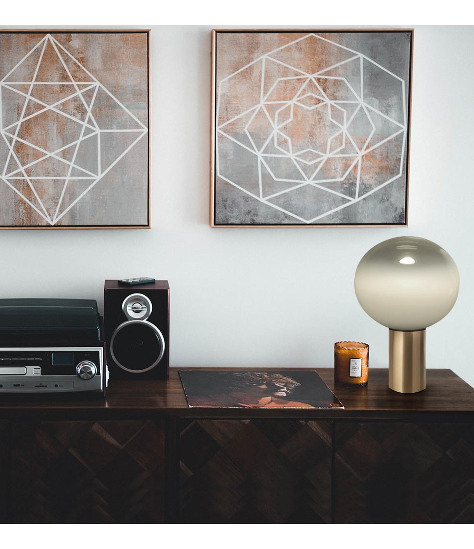 Satin brass Artemide Laguna table lamp on a console with a stereo system, beneath a painting.