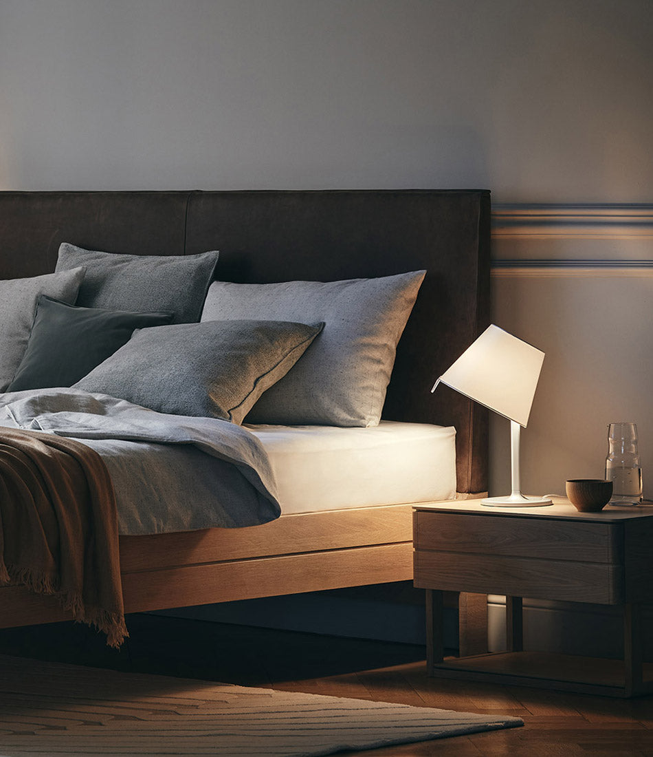 Artemide Melampo table lamp on a bedside table next to a bed.