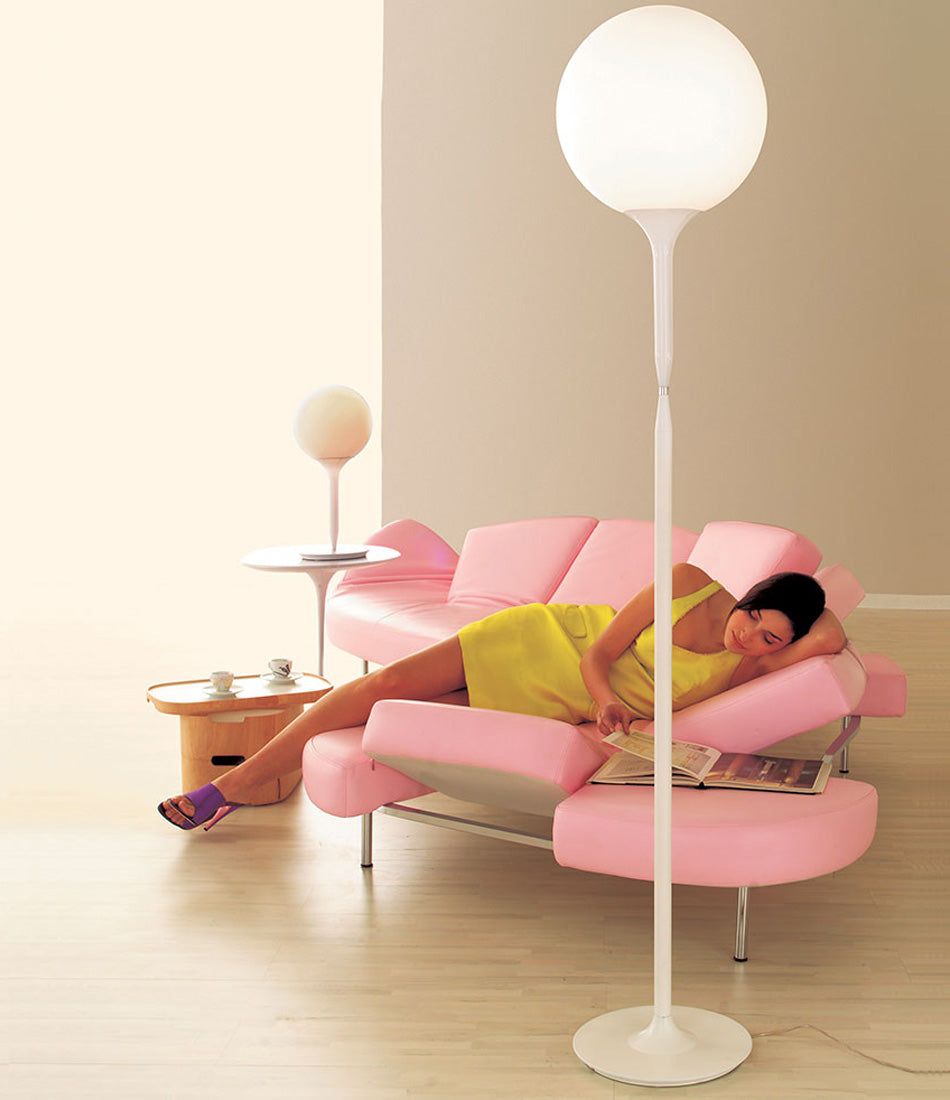 Woman reading magazine on a sofa next to Artemide Castore floor and table lamp.