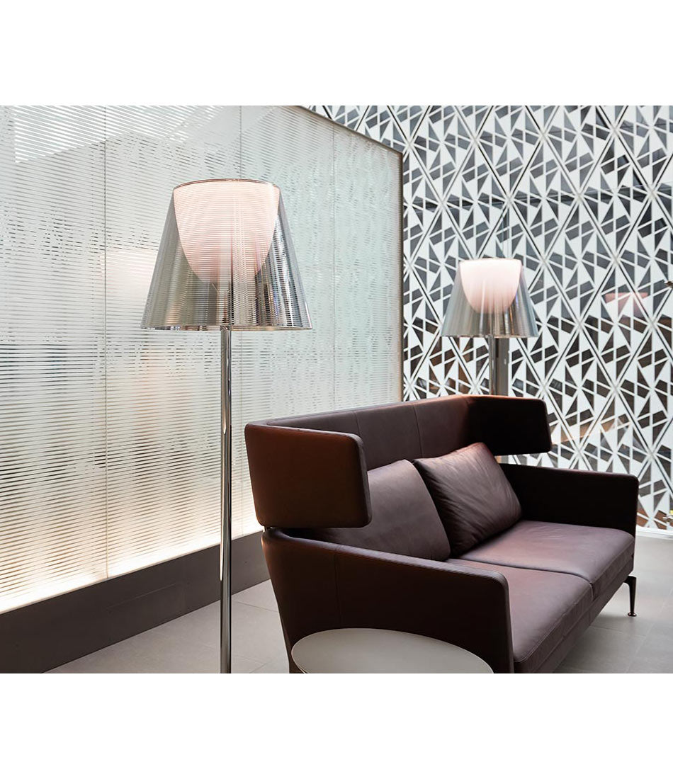 Flos KTribe floor lamp in aluminized silver next to a leather love seat.