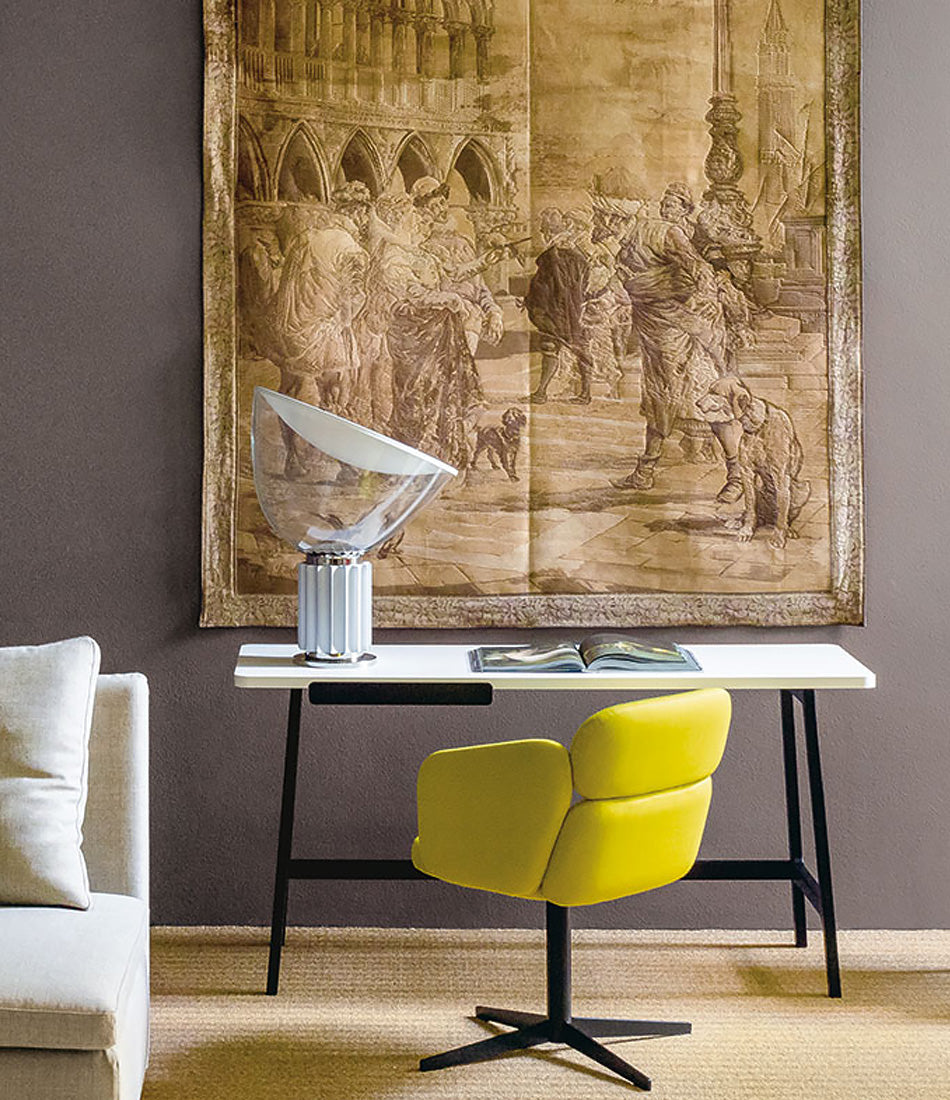 Flos Taccia table lamp on a white desk in front of a large art tapestry.